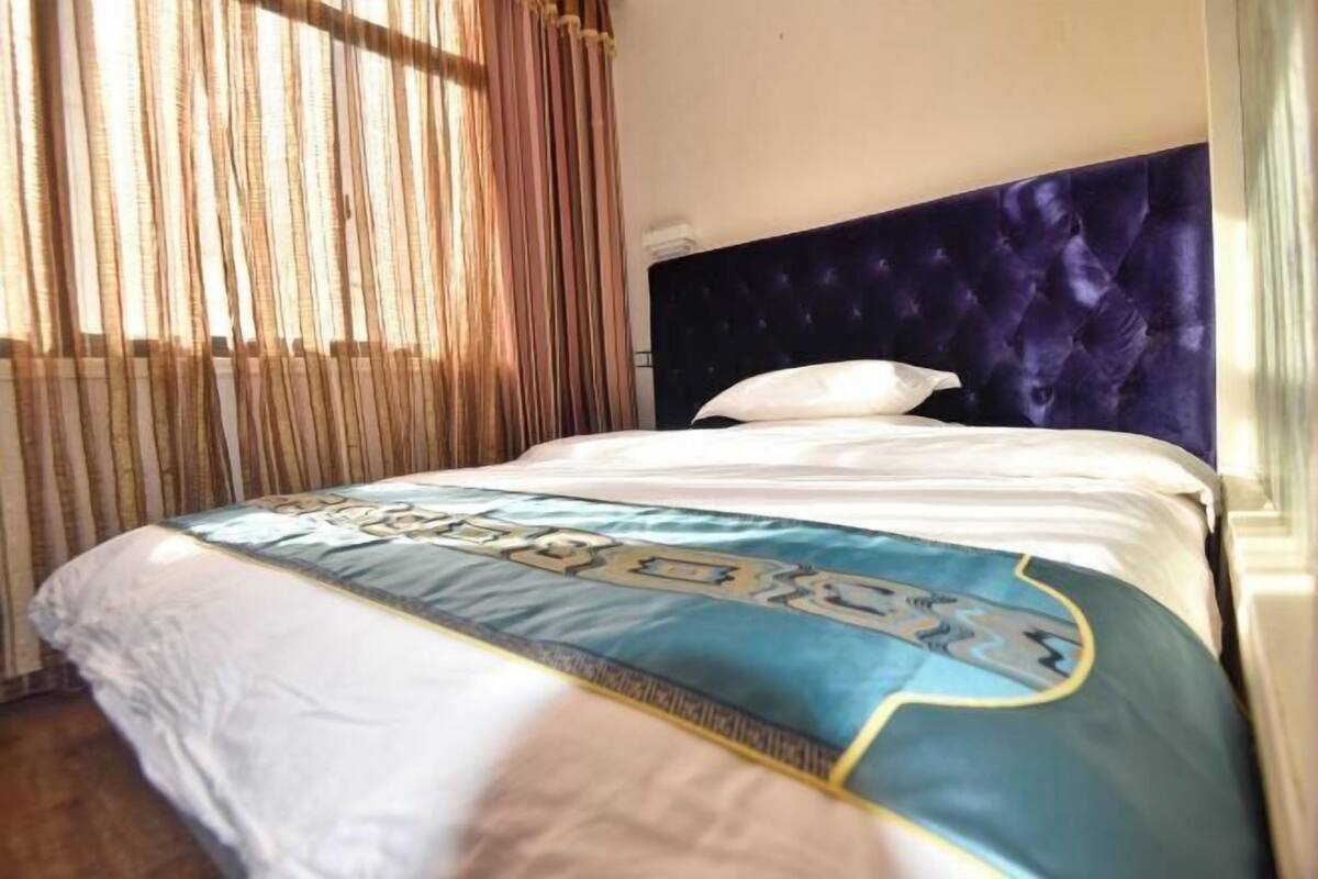 A bed with a blue and white bedspread, a dark headboard, and a window with curtains.