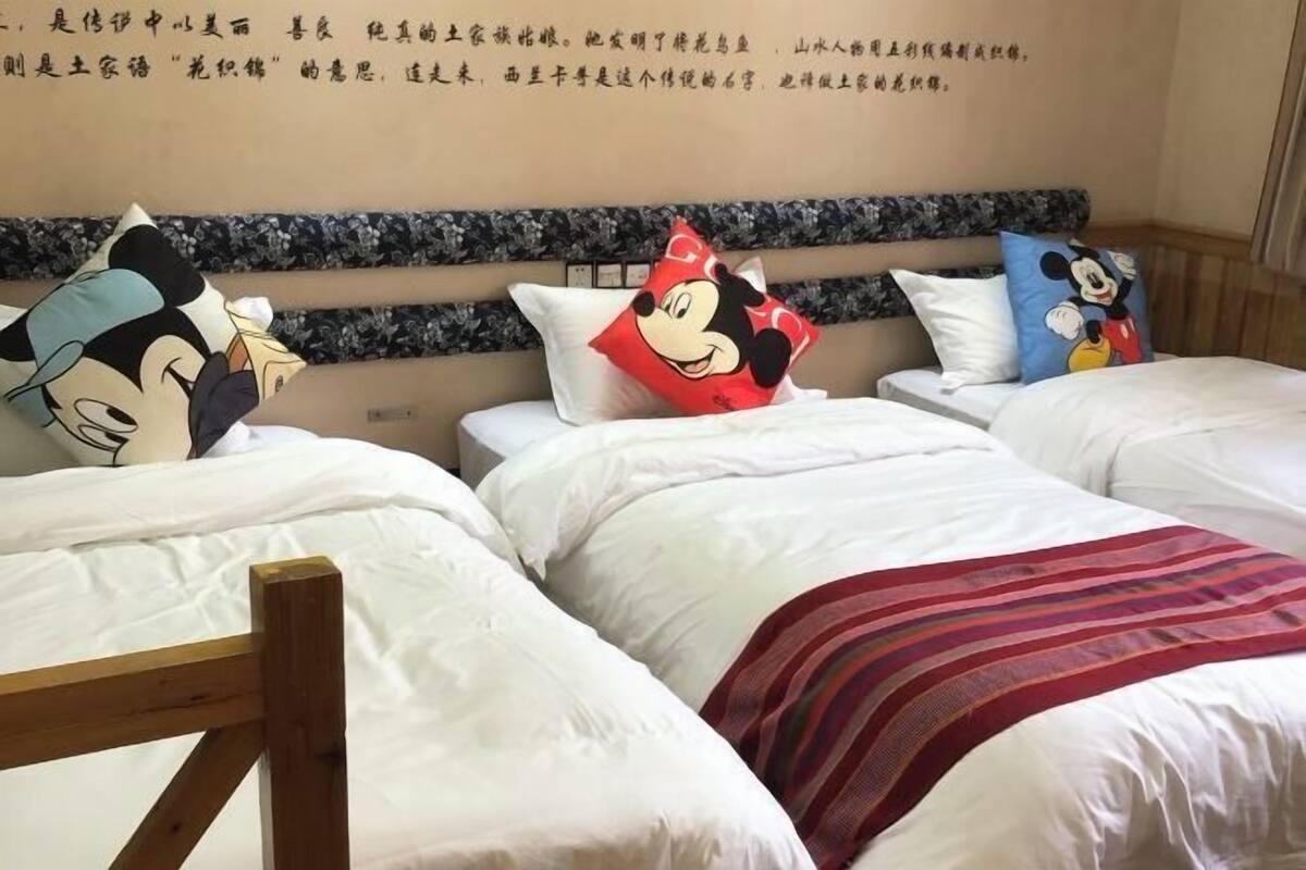 A hotel room with two beds, each with white bedding and Mickey Mouse themed pillows.