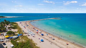 A beach with clear turquoise waters, a long stretch of sandy shore, and a pier extending into the sea.