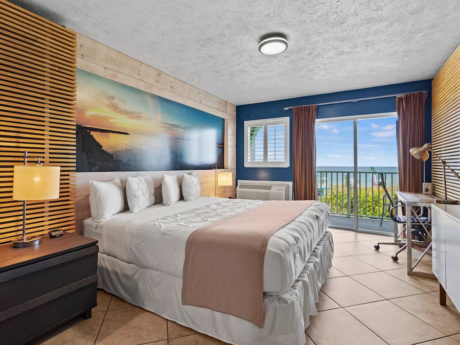 Habitación de hotel con una cama grande, un escritorio, una computadora, una ventana con cortinas y un cuadro en la pared.