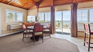 A room with a wooden ceiling, a dining table with chairs, a view of the ocean through large windows, and a balcony with curtains. - Oceanfront Inn (Fort Pierce)