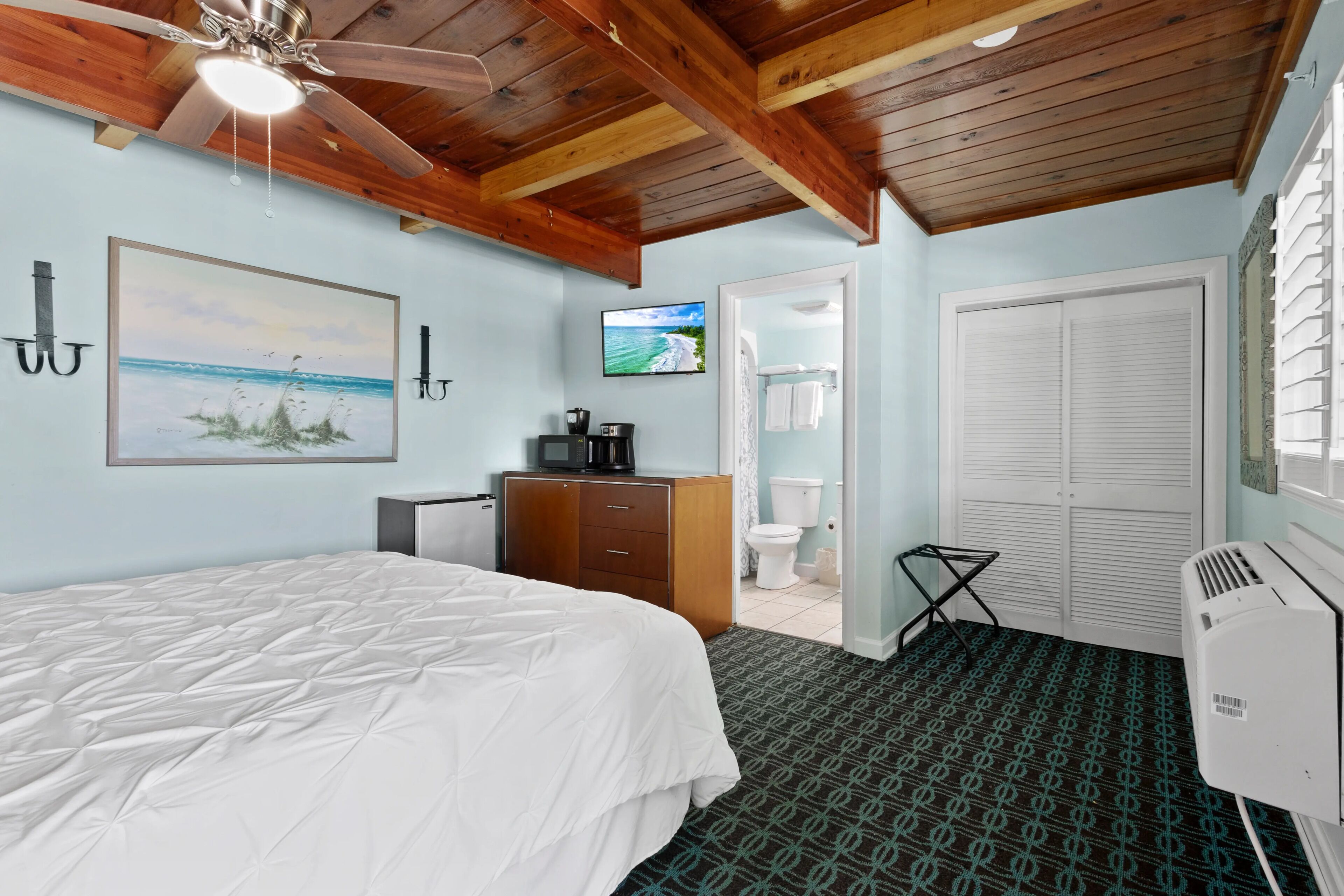 A bedroom with a bed, a television, a wardrobe, a toilet, and a ceiling fan.