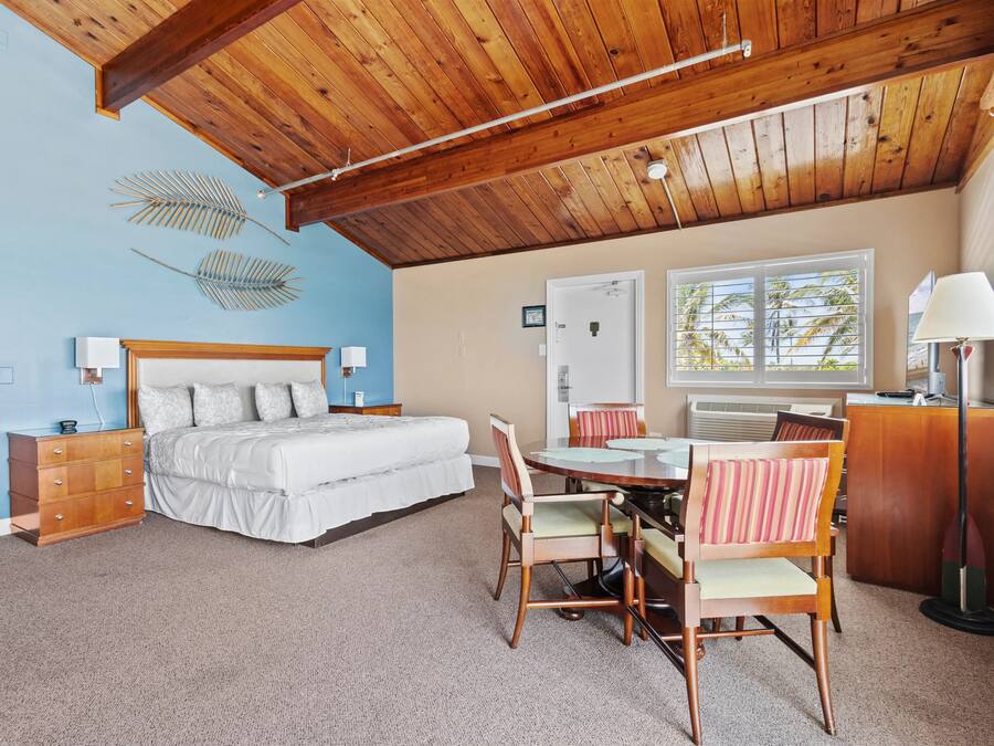 A bedroom with a bed, dresser, bedside tables, lamp, and a dining area with chairs and a table.