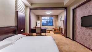 A hotel room with a bed, a desk, a chair, a television, and a window with a view. - Jindu Hotel (Wuyuan)