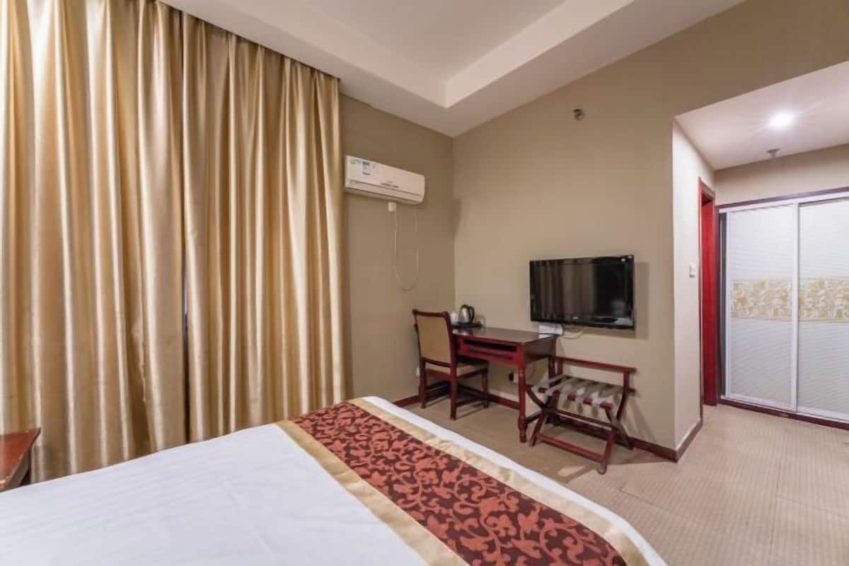 Ein Hotelzimmer mit Bett, Schreibtisch mit Stuhl, Fernseher und Klimaanlage.