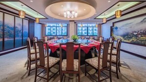 A dining area with a round table set for eight, surrounded by wooden chairs with cushioned seats. The room features large windows with a view of a mountainous landscape. - Jindu Hotel (Wuyuan)