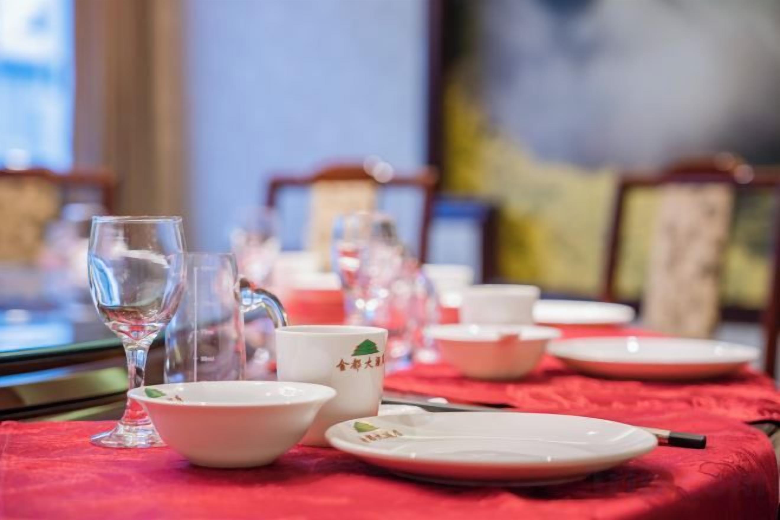 Una mesa de comedor dispuesta con platos, tazones y vasos, cubierta con un mantel rojo.