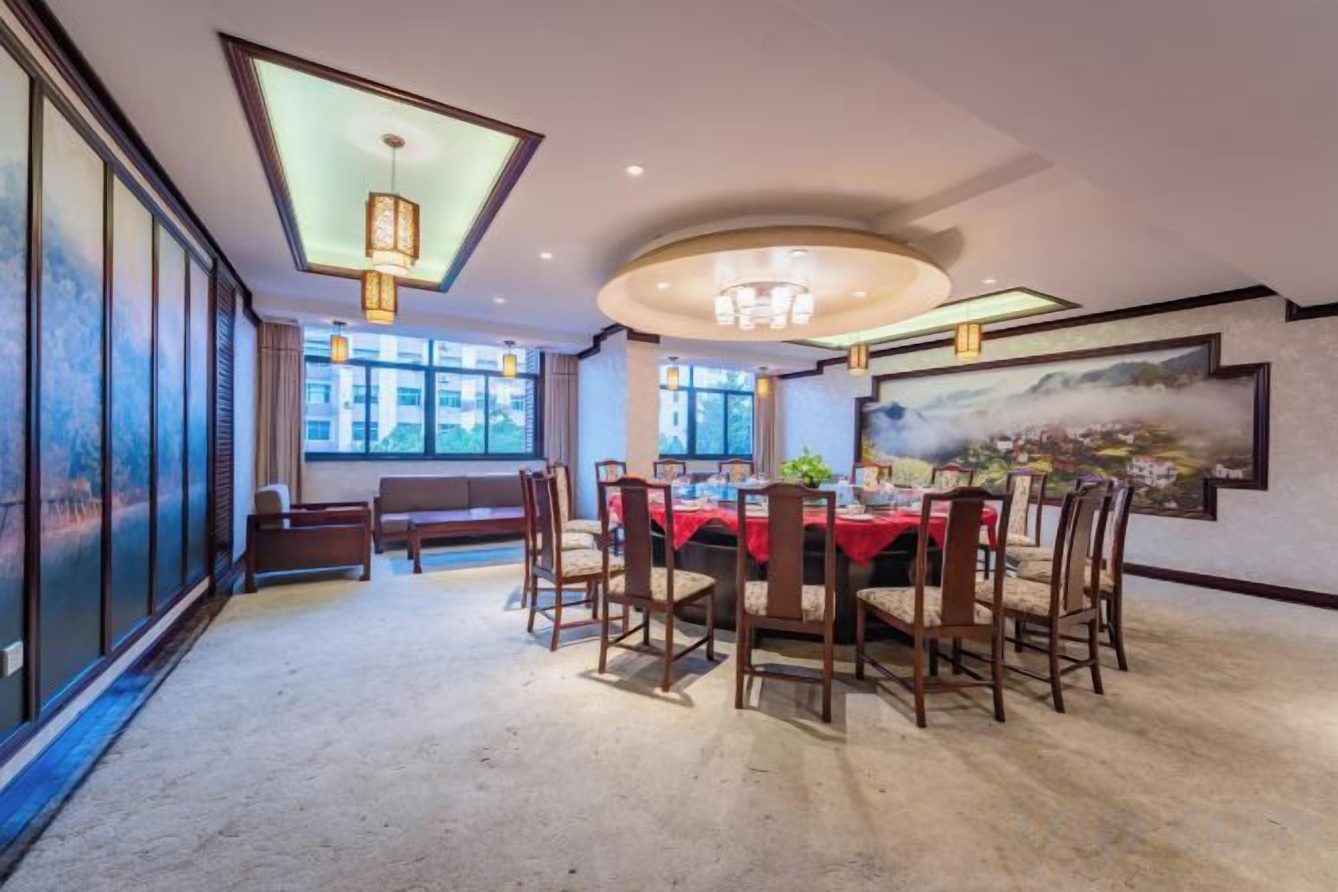 A dining area with a round table, chairs, and a red tablecloth. There are windows and a view of the outside.