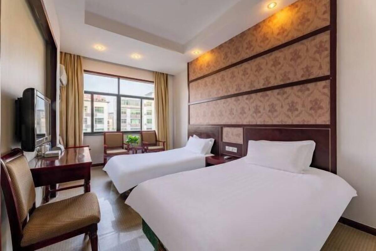 Ein Hotelzimmer mit zwei Betten, einem Schreibtisch, einem Stuhl und einem Fernseher.