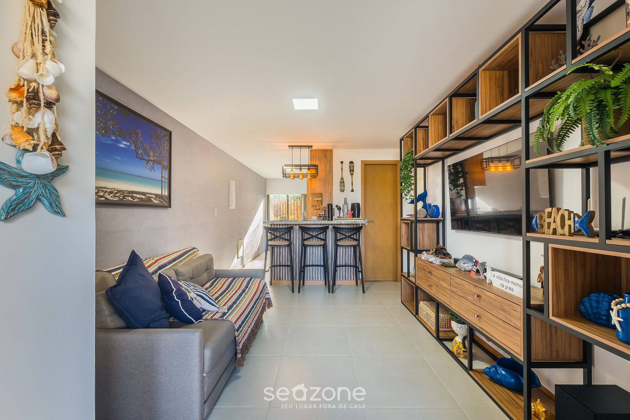 A modern living room with a sofa, a dining area with a small table and chairs, and a kitchen area with a wooden shelf unit.