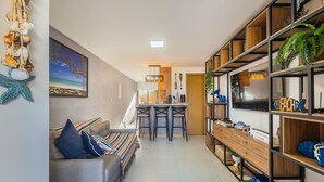 Un salon moderne comprenant un canapé, un coin repas avec une petite table et des chaises, et un espace cuisine avec une étagère en bois.