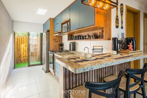 Una cocina moderna con una isla central, taburetes de bar y vistas a un área exterior verde.