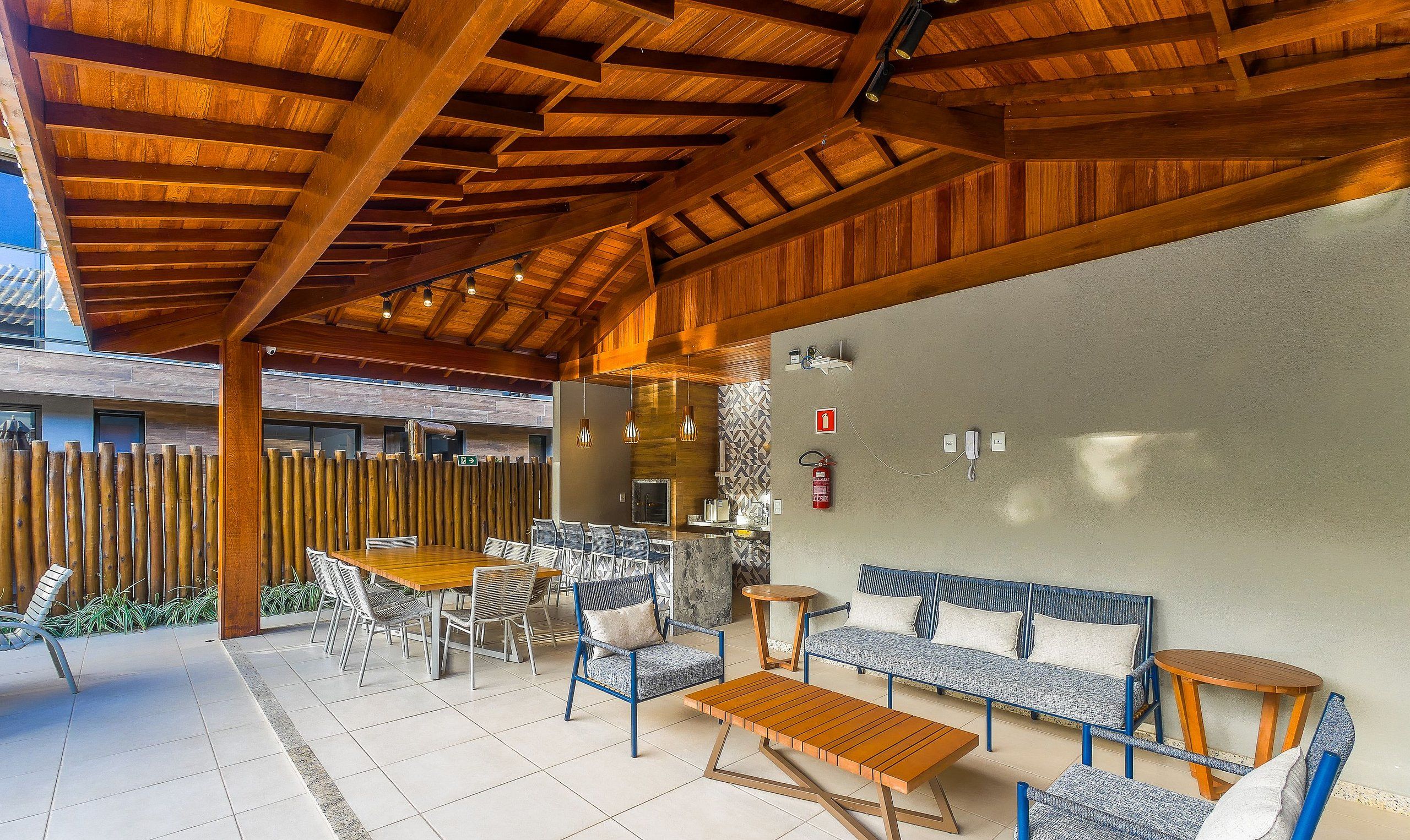 An outdoor patio with a wooden ceiling, a dining table with chairs, a sofa, and a small round table.