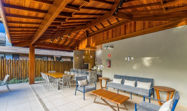 An outdoor patio with a wooden ceiling, a dining table with chairs, a sofa, and a small round table. - 2 Suite Apartment in Condo With Pool Eko0008 (Camaçari)