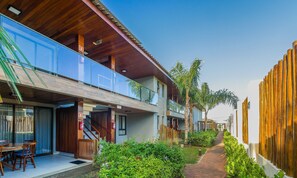 A modern building with a wooden facade, a glass balcony, and a pathway lined with greenery. - 2 Suite Apartment in Condo With Pool Eko0008 (Camaçari)