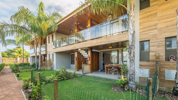 Un bâtiment moderne à deux étages, doté d’un balcon, d’un espace extérieur aménagé et couvert, et d’un jardin bien entretenu.