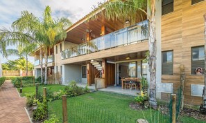 A modern two-story building with a balcony, a covered outdoor seating area, and a well-maintained garden. - 2 Suite Apartment in Condo With Pool Eko0008 (Camaçari)