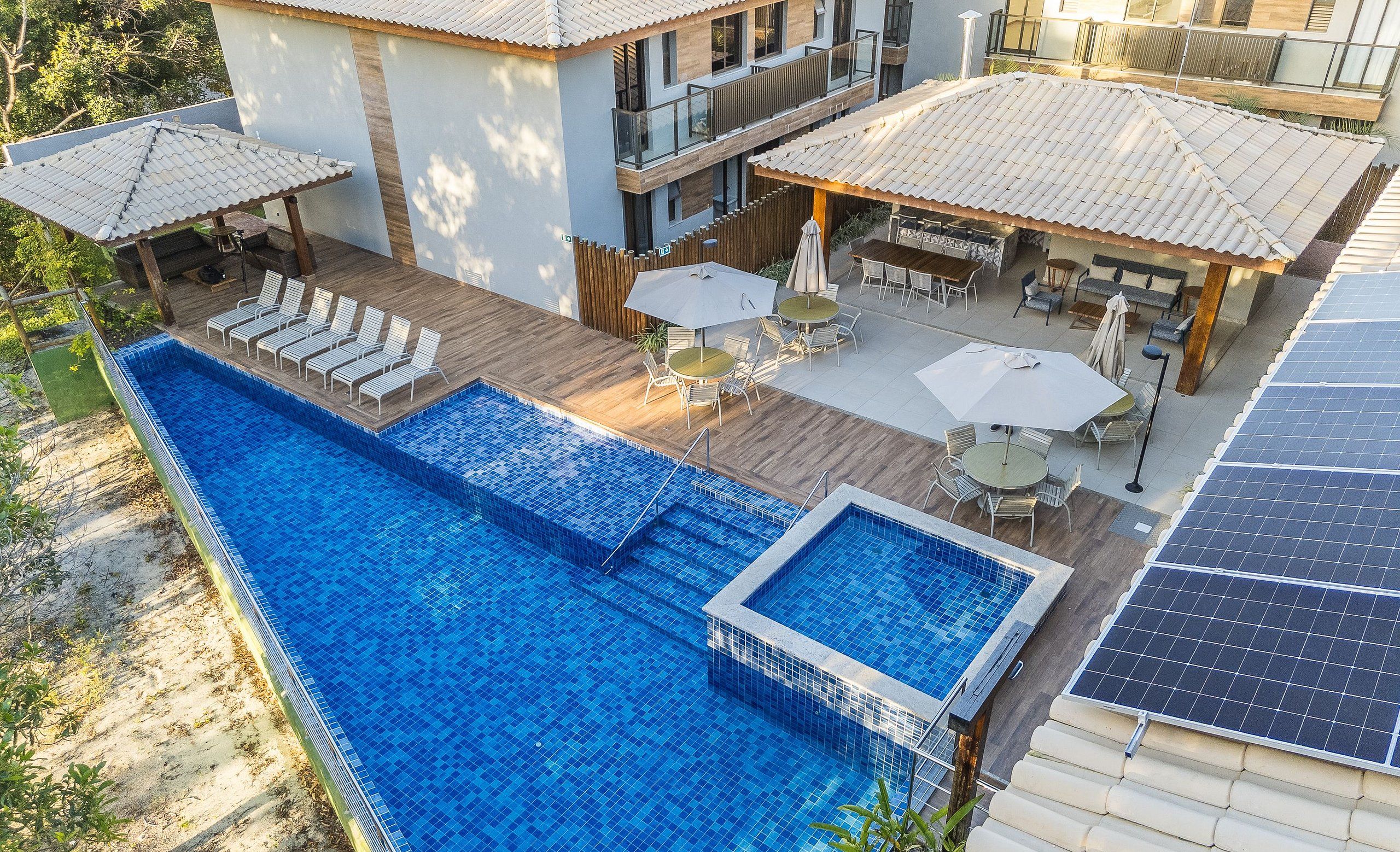 Piscina no terraço com deck de madeira, área de estar externa e painéis solares.