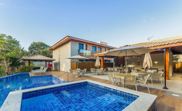 A pool area with tiled flooring, outdoor seating, and a building with a tiled roof. - 2 Suite Apartment in Condo With Pool Eko0008 (Camaçari)