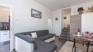 Un soggiorno moderno con un divano grigio, una zona pranzo con tavolo e sedie, una cucina con macchina da caffè e una scala che conduce a un altro piano.