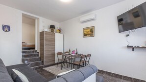 Un soggiorno moderno con un divano, un tavolo da pranzo con sedie, una TV a parete e una scala che conduce in un'altra stanza.