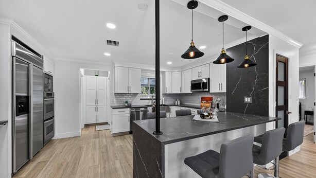 A modern kitchen with a central island, stainless steel appliances, and black pendant lighting.