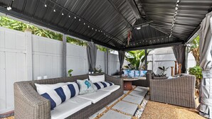 An outdoor patio with a covered seating area, stone pathway, and potted plants.