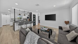 A modern living room with a grey sofa, a glass coffee table, and a TV mounted on the wall.