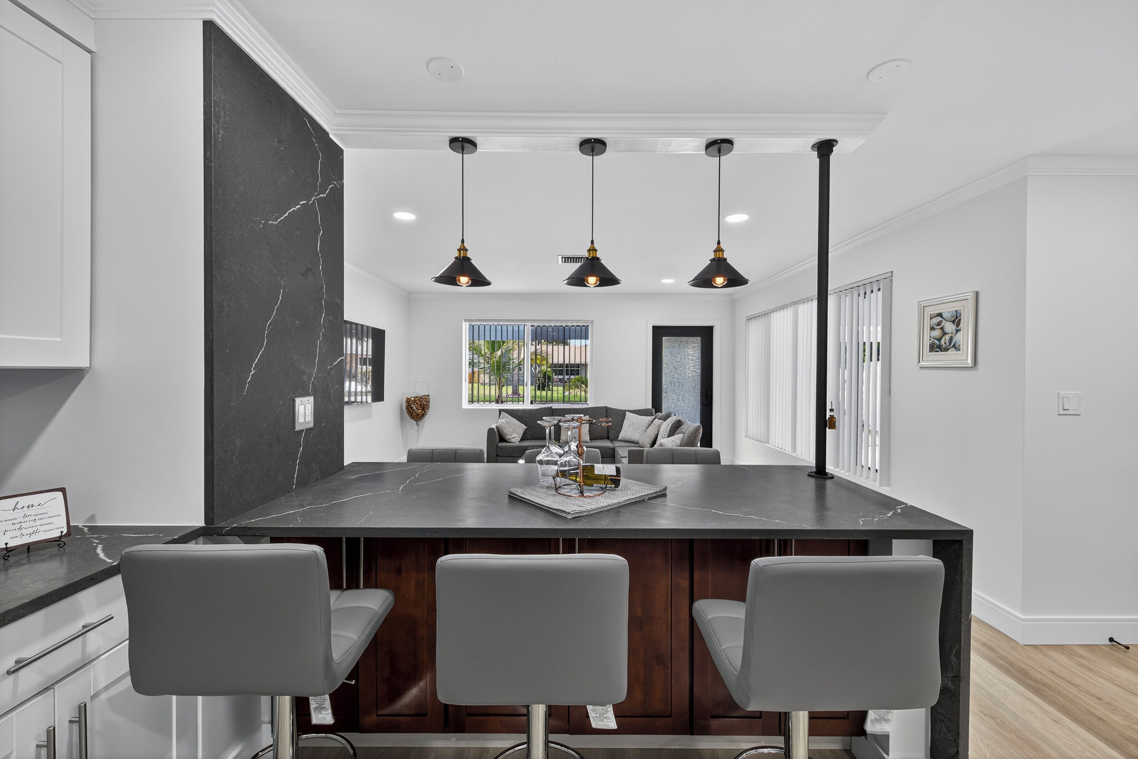 A modern kitchen with a marble island, pendant lighting, and a view to the outdoors.