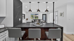 A modern kitchen with a marble island, three bar stools, pendant lighting, and a view of the outdoors.
