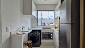 Une cuisine compacte équipée d’un lave-linge, d’un four et d’une fenêtre donnant sur un balcon.