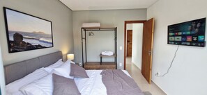 A hotel room with a bed, a TV, a painting of a rocky coastline, and a wooden door leading to a hallway. - Beautiful Complete Studio in Campeche (Campeche Florianópolis)