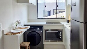 A compact kitchen with a washing machine, microwave, and refrigerator. - Beautiful Complete Studio in Campeche (Campeche Florianópolis)