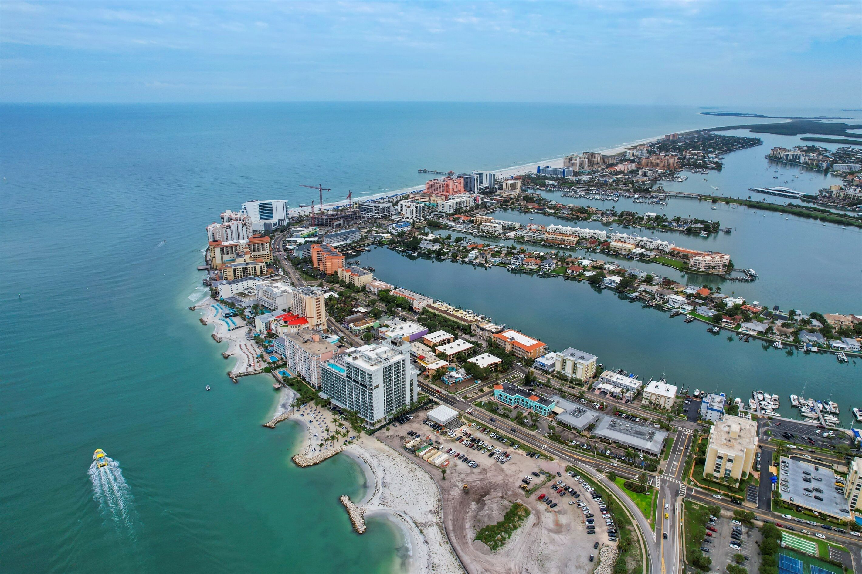 An aerial view of a coastal city with a marina, beachfront hotels, and a mix of commercial and residential buildings.