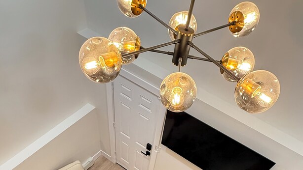 Een moderne woonkamer met een plafondlamp, een bank, een leren vloerkleed en een trap.