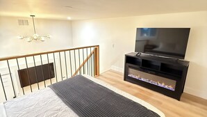 Een slaapkamer met een bed, een televisie, een open haard en een trap.
