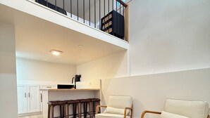 Een ruime woonkamer met een hoge plafond, een trap, een keukenhoek en een groot vloerkleed.
