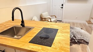 Een moderne keuken met een houten aanrecht, een roestvrijstalen spoelbak en een inductiekookplaat. Er zijn witte kasten met zwarte handgrepen en een witte deur op de achtergrond.