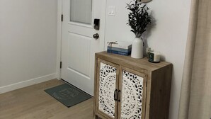 Une porte blanche avec un panneau « Interdiction de fumer », un miroir décoratif, un meuble en bois orné de sculptures complexes et une petite plante posée sur le dessus.