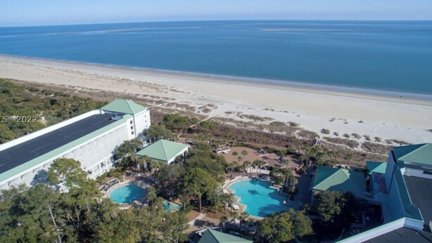 An aerial view of a resort with multiple swimming pools, a large building with a green roof, and a beach in the background.