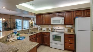 A modern kitchen with granite countertops, wooden cabinets, a white refrigerator, a microwave, an oven, and a coffee maker.
