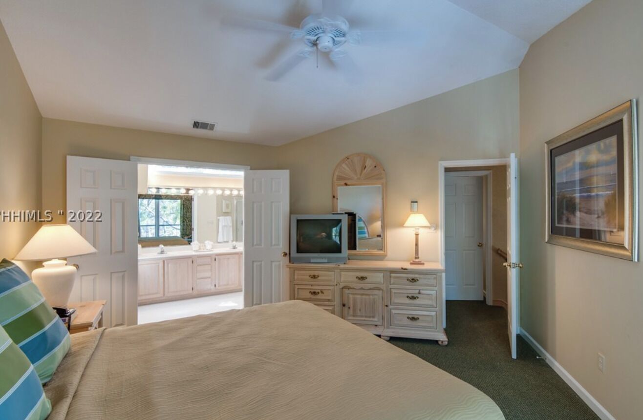 A bedroom with a bed, a television, a dresser, and a door leading to a bathroom.