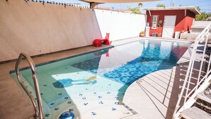 En swimmingpool med fliseterrasse, metalstige og en rød legekonstruktion.
