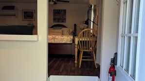 Een slaapkamer met een bed, een stoel, een nachtkastje, een wandlamp en een brandblusser.