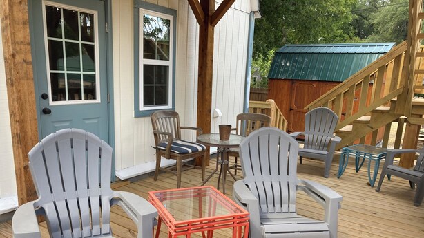Een houten terras met grijze Adirondack-stoelen, een glazen tafel en een blauwe deur.