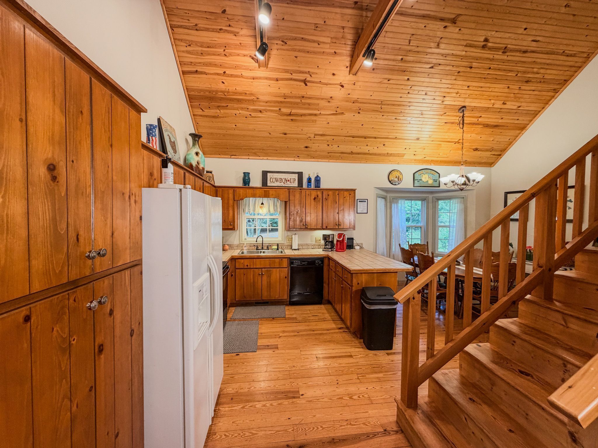 A kitchen with wooden cabinets, a refrigerator, a sink, and a staircase leading to another level.