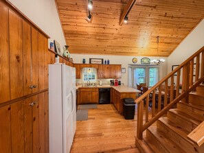 A kitchen with wooden cabinets, a refrigerator, a sink, and a staircase leading to another level.