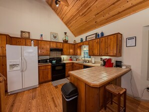 A kitchen with wooden cabinets, a white refrigerator, a stove, and a tiled island.
