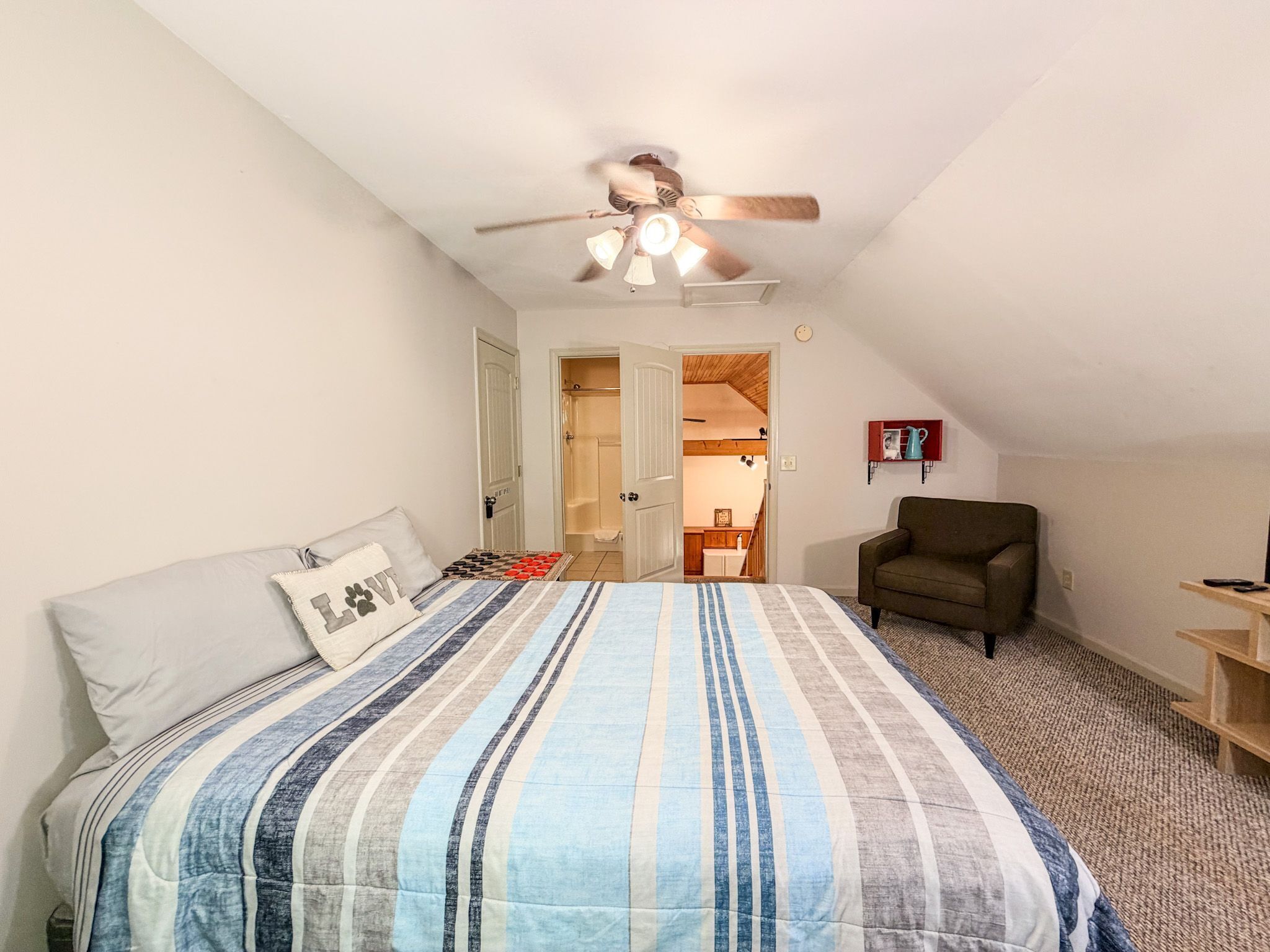 Ein Schlafzimmer mit einem Bett, einem Sessel, einem Deckenventilator und einer Tür zu einem Badezimmer.