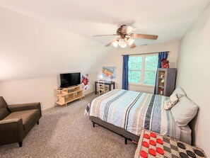 A bedroom with a bed, a TV, a ceiling fan, a window with curtains, and a bookshelf.